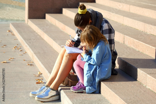 the woman with the little girl drawing in a notebook while sitting on the stairs