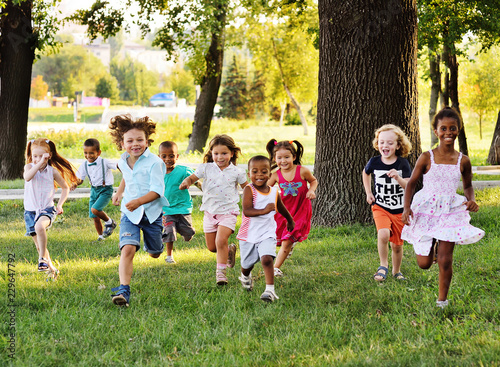 A group of happy children of boys and girls run in the Park on the grass on a Sunny summer day . The concept of ethnic friendship, peace, kindness, childhood. photo