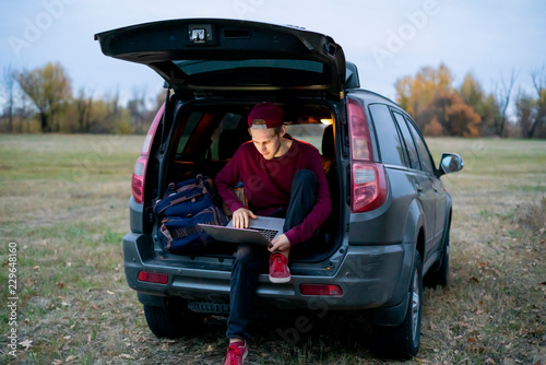young freelancer website creator sitting in the car trunk with laptop and working in the trip f © Mihail