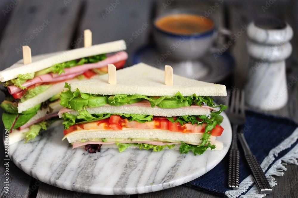Fresh tasty sandwich with lettuce, ham, cheese, avocado, and tomato. English breakfast Fresh tasty sandwich with lettuce, ham, cheese, avocado, and tomato. English breakfast