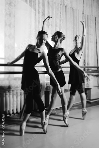 three young cute ballerinas perform exercises on a choreographic machine or barre on the background of a ballet class