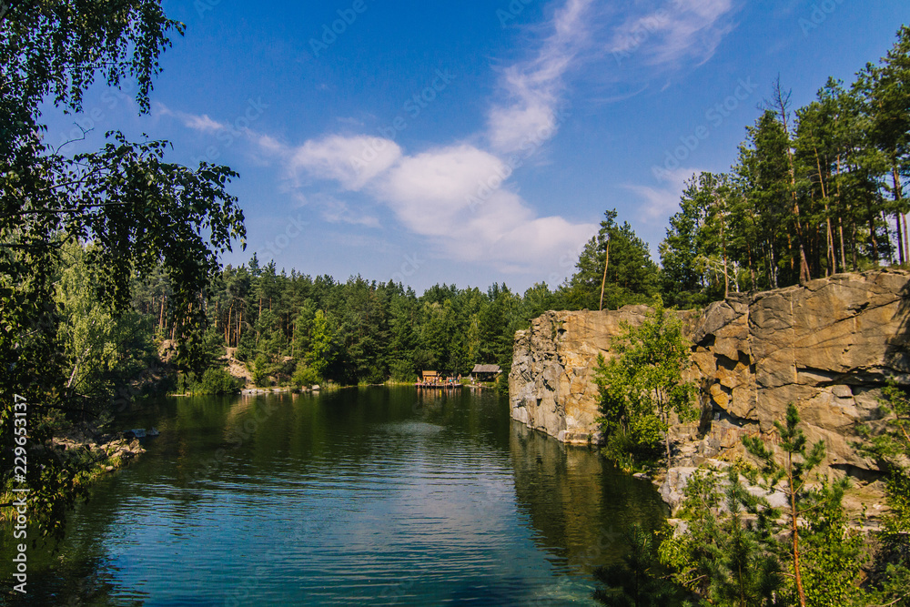 Korostyshiv Canyon, deep lake in Zhytomir region with green water and blue sky in Ukraine and fir forest around
