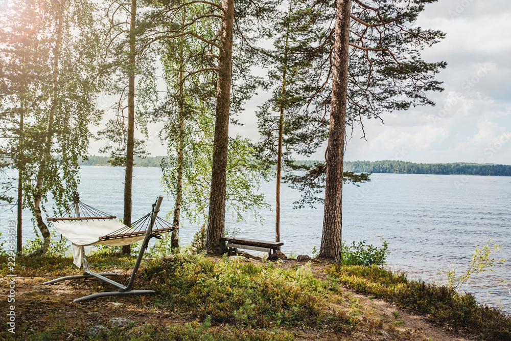 A hammock and a bench on the shore of a lake in the forest in the sun, freelance concept, holiday wallpaper. A hammock and a bench on the shore of a lake in the forest in the sun, freelance concept, holiday wallpaper.