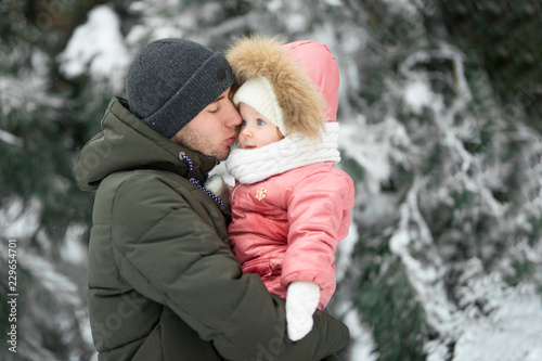 Dad and daughter kissing daughter in a snowy forest, with empty space