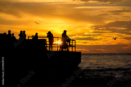Fishermen and photographers silhouetted against a setting sun.