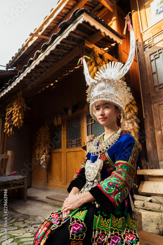 Young Miao woman in traditional dress and headdress sitting outdoors photo