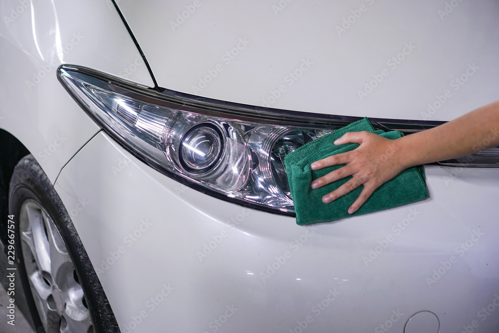 hand cleaning car headlight on a white car