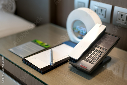 Black telephone and note in front and bed in the background, focus on the telephone,for room service,communication themes in hotel or resort..