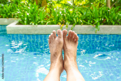 old woman feet, in soft focus, with blurred pool background and green tree