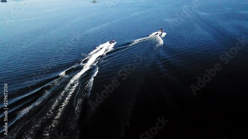 4K aerial shot of motor boats speeding along a blue lake on a sunny day. photo