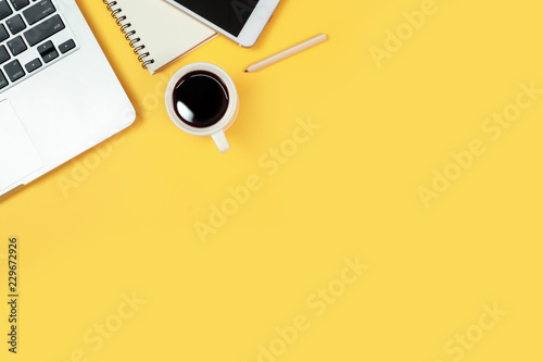 workspace table with laptop computer, office supplies, coffee cup, cell phone and coffee cup on yellow background