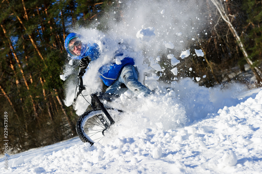 Naklejka premium Extreme cyclist riding bicycle near snowbanks of mountain slope, winter sport, cross country biking near forest in cool sunny day 