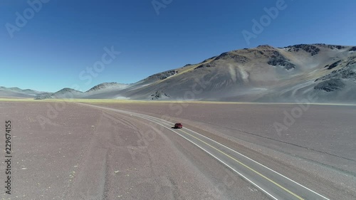 Aerial drone scene of van traveling over road between rocky eroded colorfull mountains with yellow vegetation in front. Catamarca, Argentina. General view of landscape. photo