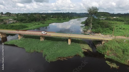 The Mbalmayo bridge can be seen from up high with cars and off-road vehicles driving by. the blue sky and the forest background are clearly visible. photo