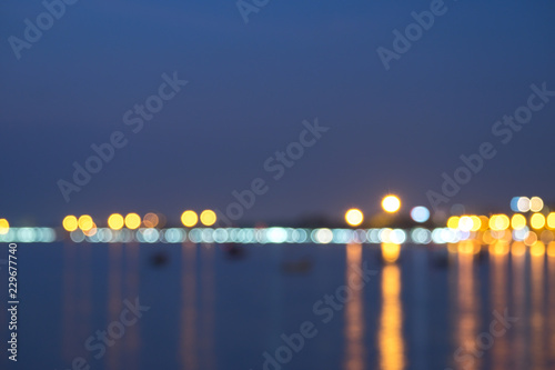 Colorful night bokeh light at the sea with city skyline defocused background.