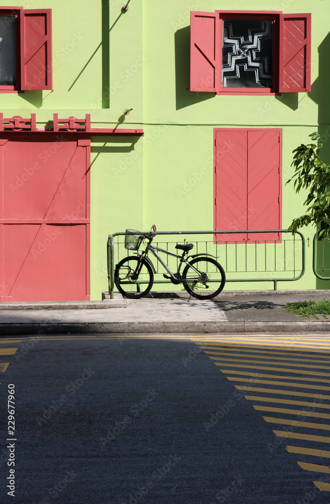 Black Bike with basket standing in front of a colourful green house with red windows at Clarke Quay in Singapore