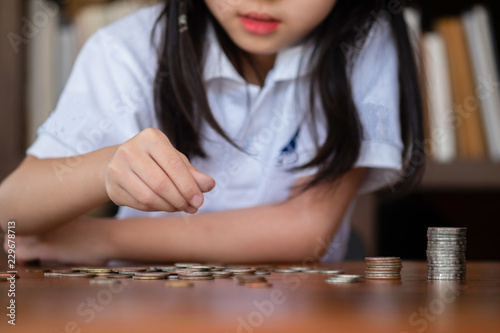 cute girl sitting in library putting money coin to stack on table,saving money concept