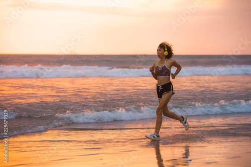fit and athletic Asian Chinese sporty woman running on beautiful beach doing jogging workout on sunset in fitness healthy lifestyle and summer outdoors activity