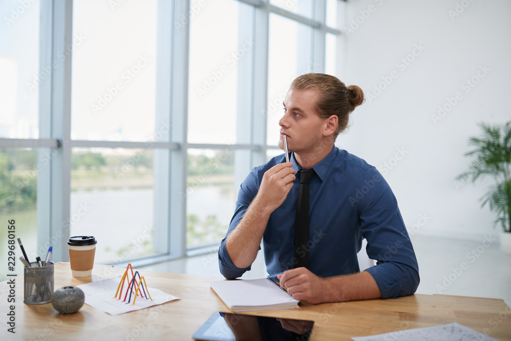 Pensive young engineer looking through office window Pensive young engineer looking through office window