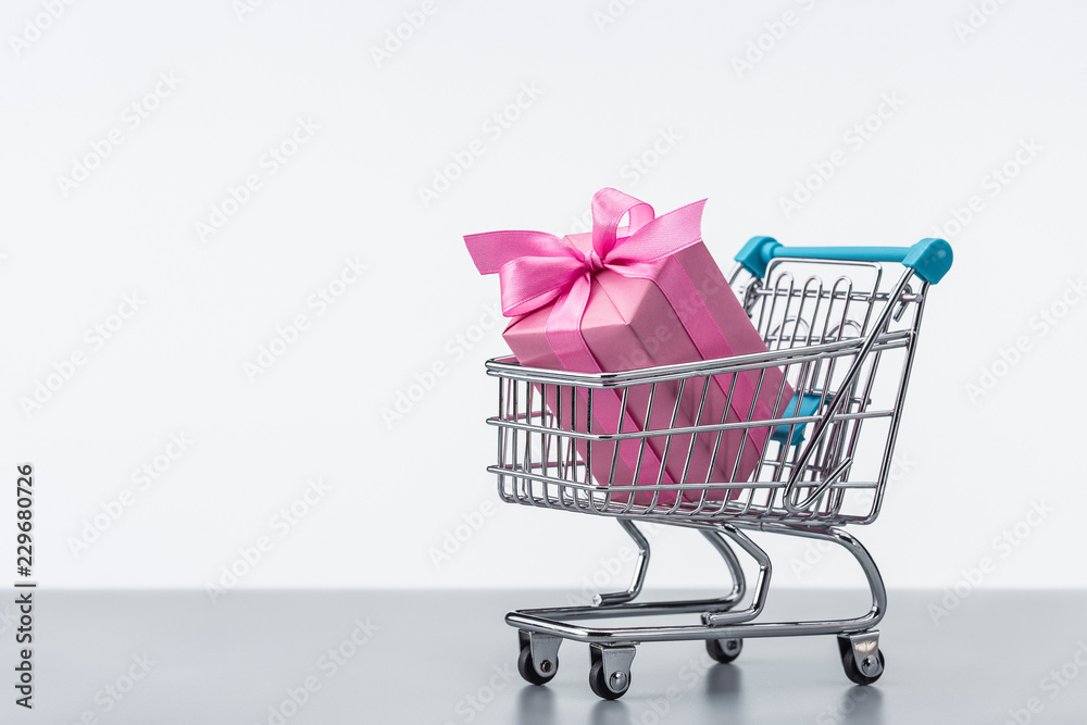 Gift box, in pink packaging, decorated with ribbons and bows in shopping cart.