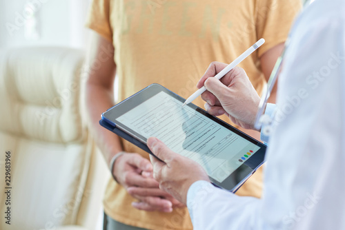 Doctor filling medical card on digital tablet when talking to patient photo