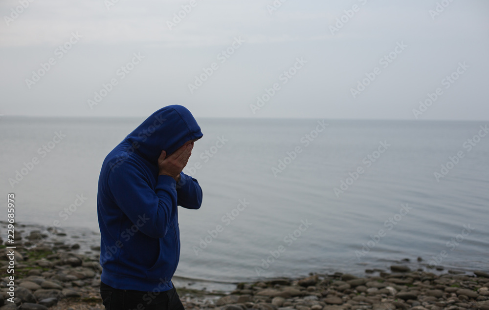 Lonely Young Man in a Hoodie Standing on the Sea Background. Gloomy Weather.