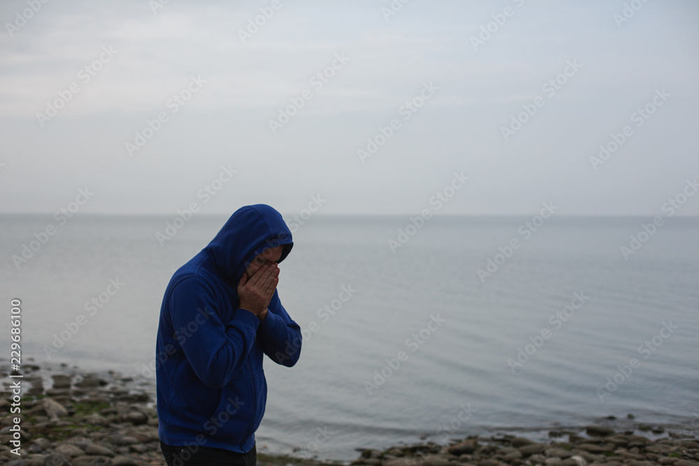 Lonely Young Man in a Hoodie Standing on the Sea Background. Gloomy Weather