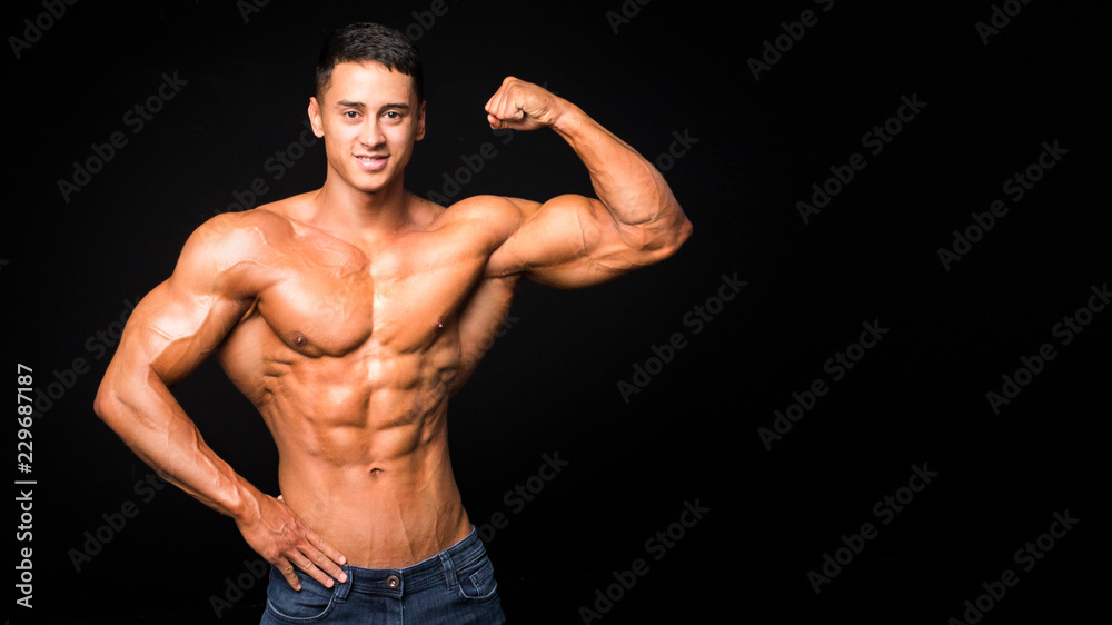 Young handsome sportsman bodybuilder weightlifter with an ideal body, after coaching poses in front of the camera, abdominal muscles, biceps triceps chest.