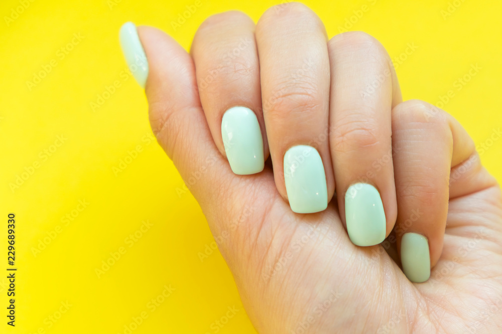 Tender hands with perfect blue manicure on trendy pastel yellow background. Place for tex Tender hands with perfect blue manicure on trendy pastel yellow background. Place for tex
