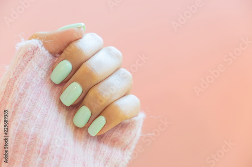Tender hands with perfect blue manicure on trendy pastel pink background. Place for tex