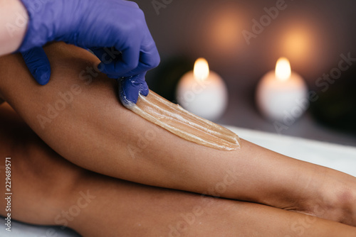 Midsection of beautician waxing woman's leg at salon photo