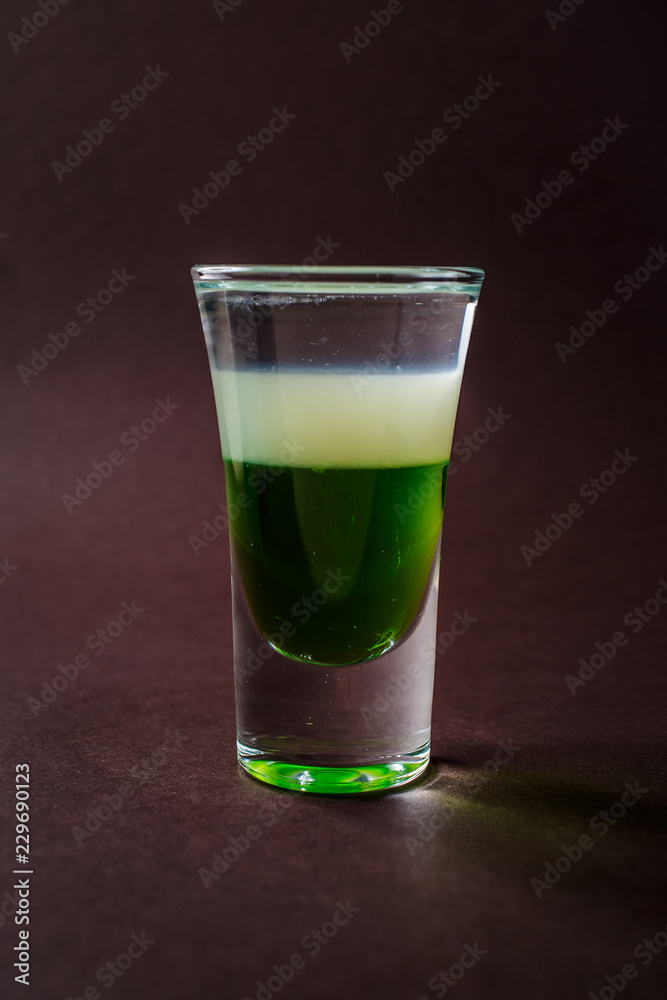 Green mexican alcoholic shot glass with tequila on elegant dark brown background Green mexican alcoholic shot glass with tequila on elegant dark brown background