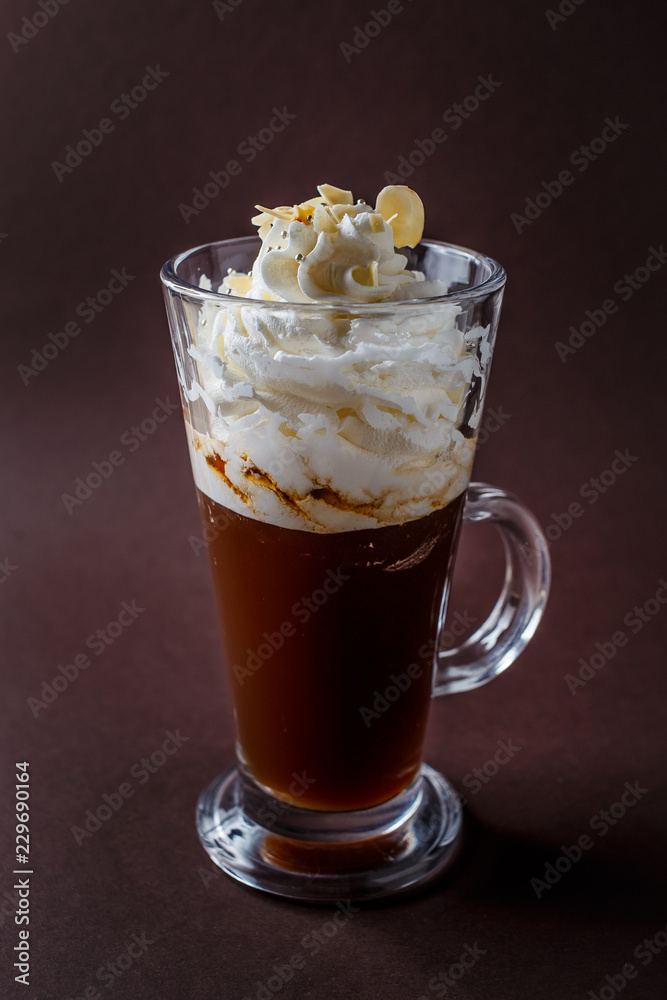 Glass of frappucino with whipped cream and almonds shaving on elegant dark brown background Glass of frappucino with whipped cream and almonds shaving on elegant dark brown background