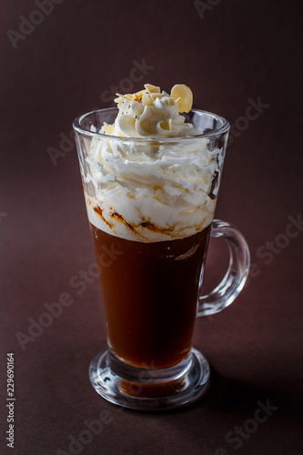 Glass of frappucino with whipped cream and almonds shaving on elegant dark brown background