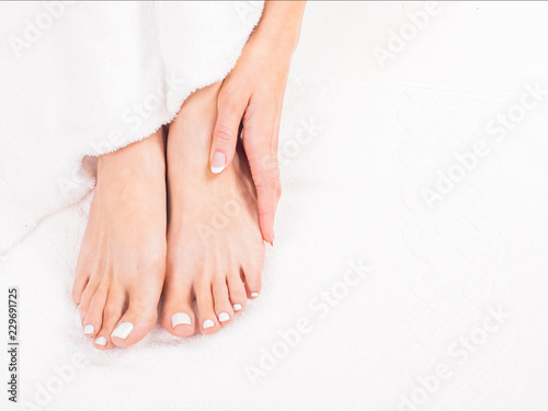 Woman Holding her Tired Feet in Hand Sitting on white terry towel.