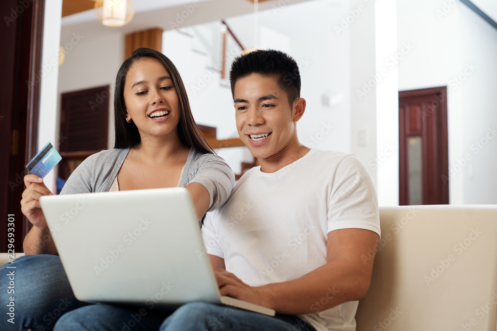 Joyful young mixed-race couple with credit card shopping online