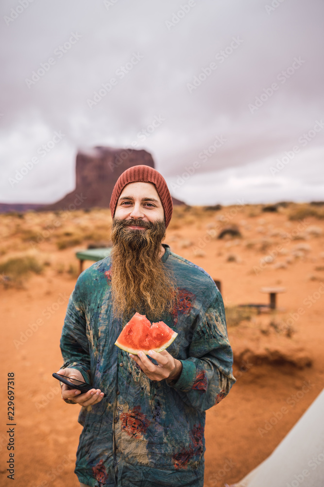 Fototapeta premium Cheerful guy with watermelon and smartphone in nature