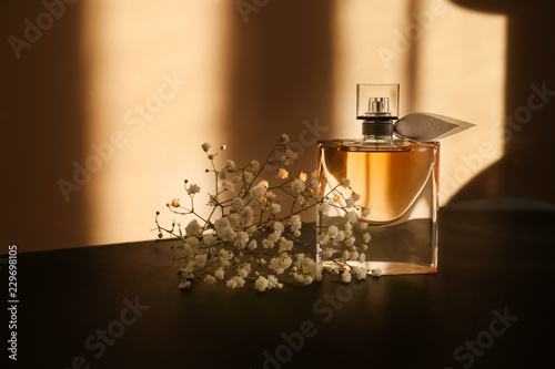 Transparent bottle of perfume with beautiful flowers on dark table photo
