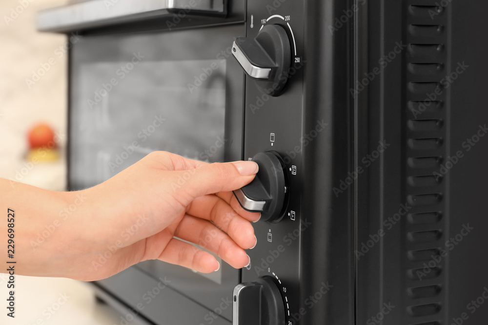 Naklejka premium Woman adjusting electric oven in kitchen
