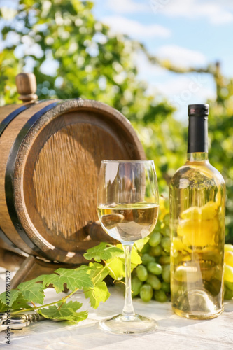 Barrel, glass and bottle of white wine on table in vineyard