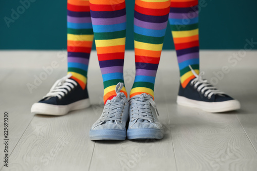 Legs of young lesbian couple in rainbow stockings standing against color wall