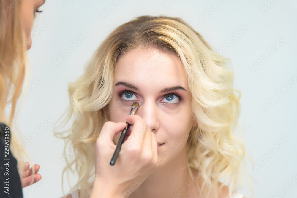 The work of a professional make-up artist, beautician, makes makeup on the face of a blonde girl with shadows on the eyes. The work of a professional make-up artist, beautician, makes makeup on the face of a blonde girl with shadows on the eyes.