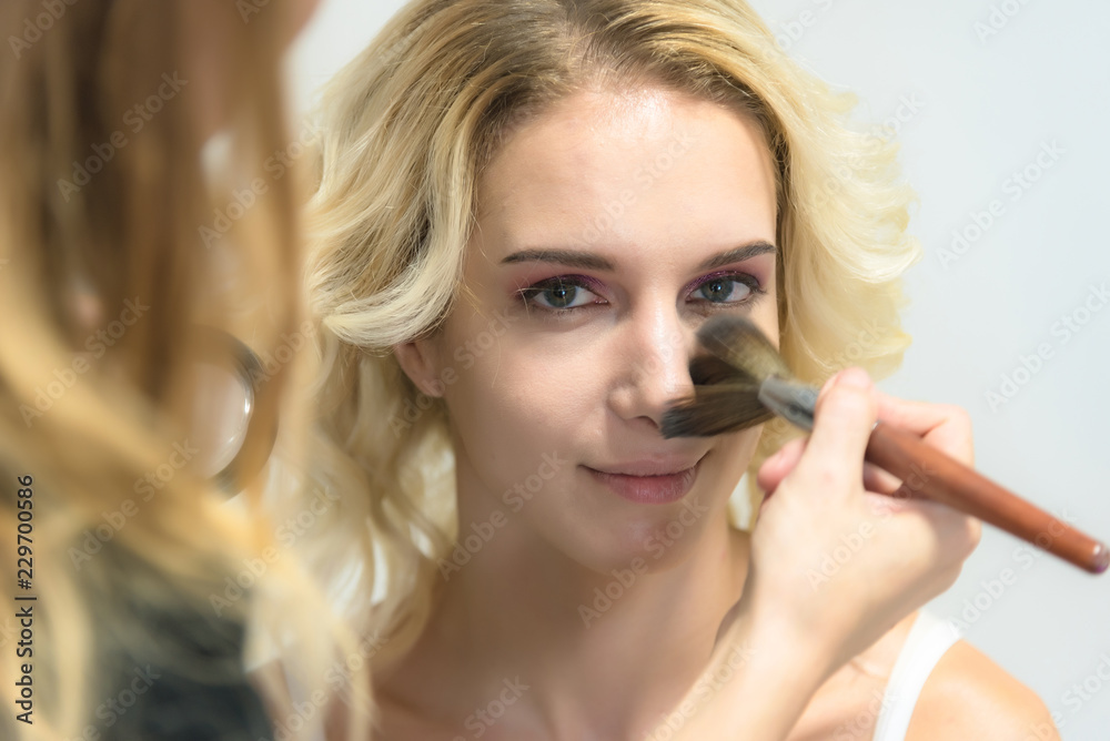 Fototapeta premium The work of a professional make-up artist, beautician, makes makeup on the face of a blonde girl with shadows on the eyes.