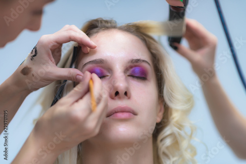 The work of a professional make-up artist, beautician, makes makeup on the face of a blonde girl with shadows on the eyes.
