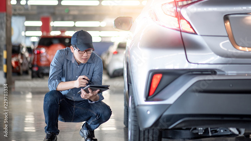 Young Asian auto mechanic holding digital tablet checking car wheel in auto service garage. Mechanical maintenance engineer working in automotive industry. Automobile servicing and repair concept