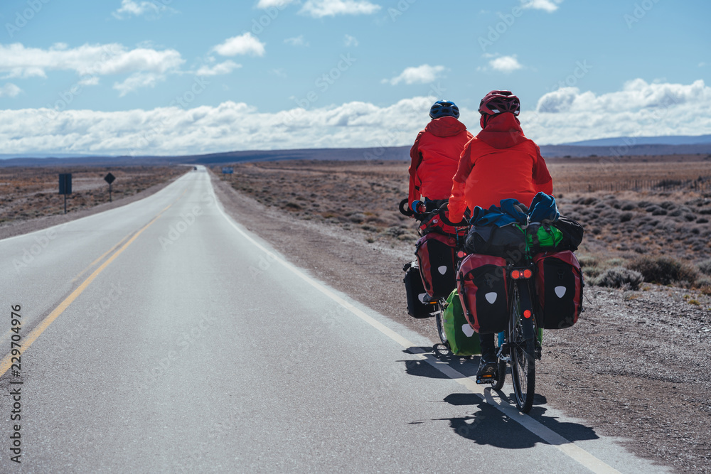 Two cyclists with baggage on the road horizon  