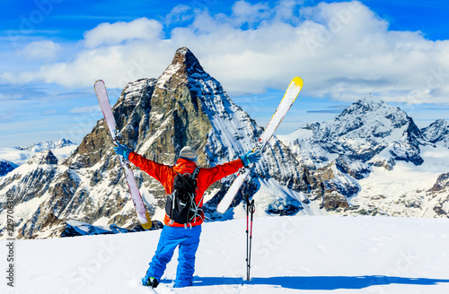 Man skiing on fresh powder snow. Ski in winter season, mountains and ski touring backcountry equipments on the top of snowy mountains in sunny day with Matterhorn in background, Zermatt in Swiss Alps.