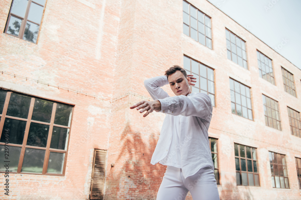low angle view of young male dancer in white clothes dancing on street
