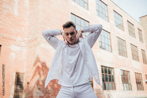 low angle view of handsome young man in white clothes dancing on urban street
