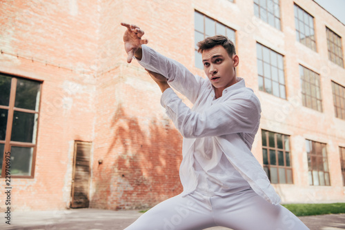 young male dancer in white clothes dancing on city street
